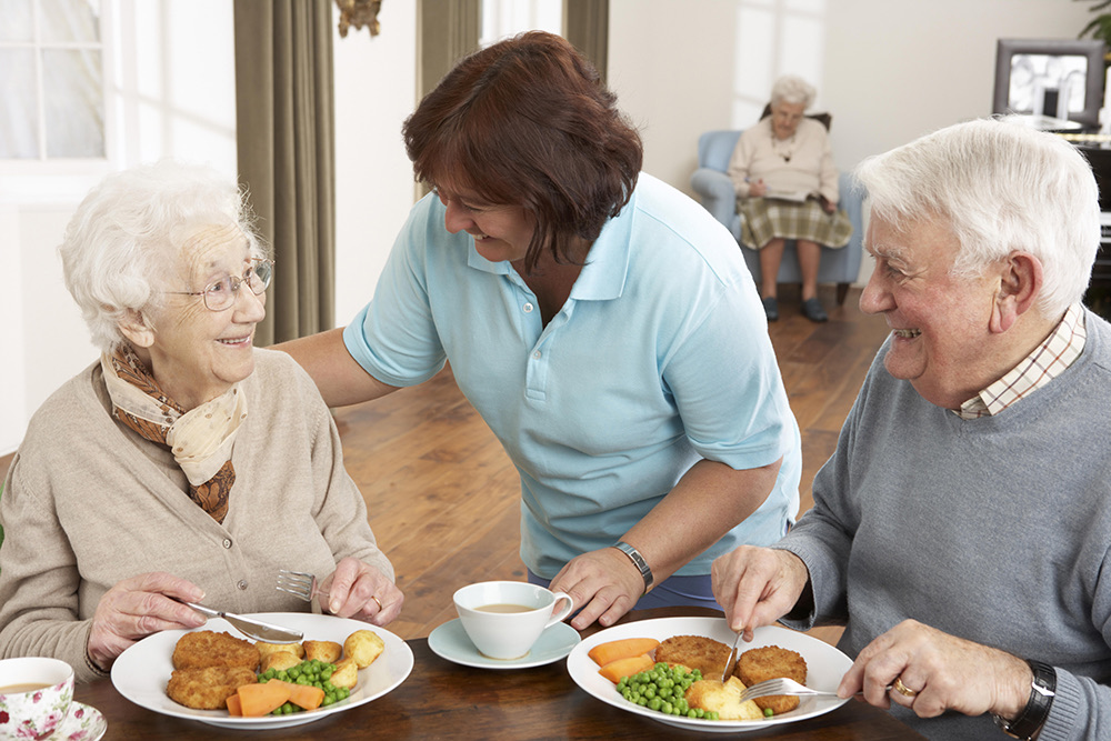 A caregiver sharing a meal with two residents at an Advinia Care community